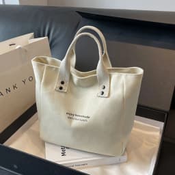 A Casual Canvas Tote Bag with a Bell Pendant and Zipper Closure; This Stylish and Durable Tote Bag Is Perfect for School and Work