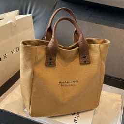 A Casual Canvas Tote Bag with a Bell Pendant and Zipper Closure; This Stylish and Durable Tote Bag Is Perfect for School and Work
